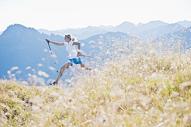 Österreich, Bundesland Salzburg, Junge Frau mit Nordic-Walking-Stock und Springen auf einer Almwiese - HHF004044