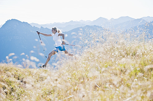 Austria, Salzburg County, Young woman with nordic walking pole and jumping in alpine meadow - HHF004044