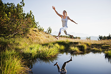 Austria, Salzburg County, Young woman jumping over mountain lake - HHF004049