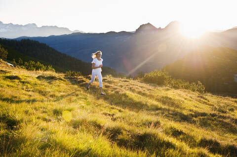 Österreich, Land Salzburg, Junge Frau läuft auf einer Almwiese, lizenzfreies Stockfoto