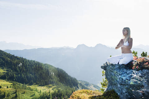Austria, Salzburg County, Young woman sitting on rock and doing meditation stock photo