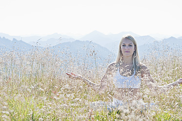 Austria, Salzburg County, Young woman sitting in alpine meadow and doing meditation - HHF004061