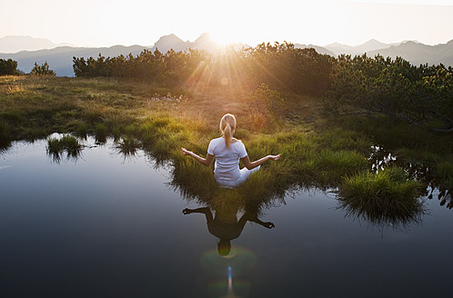 Austria, Salzburg County, Young woman sitting near mountain lake and doing meditation - HHF004068