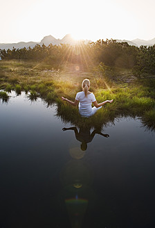 Austria, Salzburg County, Young woman sitting near mountain lake and doing meditation - HHF004069