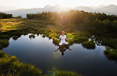 Österreich, Land Salzburg, Junge Frau sitzt am Bergsee und meditiert - HHF004071