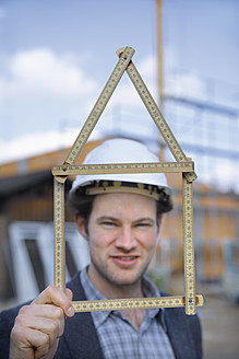 Deutschland, Bayern, Junger Mann mit Schutzhelm und Zollstock auf einer Baustelle - TCF002366