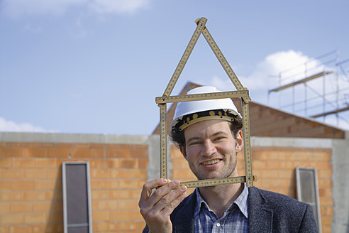 Deutschland, Bayern, Junger Mann mit Schutzhelm und Zollstock auf einer Baustelle - TCF002364