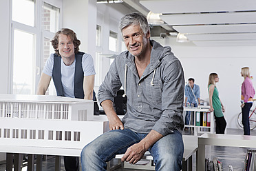 Deutschland, Bayern, München, Männer mit Architekturmodell im Büro, Kollegengespräch im Hintergrund - RBYF000014