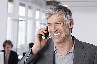 Germany, Bavaria, Munich, Mature man on mobile phone, colleagues working in background - RBYF000096