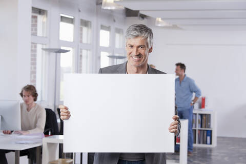 Deutschland, Bayern, München, Älterer Mann hält Plakat im Büro, lizenzfreies Stockfoto