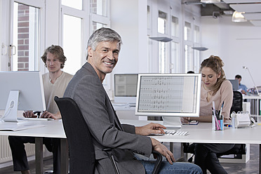 Germany, Bavaria, Munich, Mature man smiling, colleagues working in background - RBYF000103