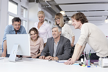 Germany, Bavaria, Munich, Men and women using computer in office, smiling - RBYF000104