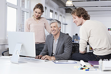 Germany, Bavaria, Munich, Men and woman using computer in office, smiling - RBYF000105