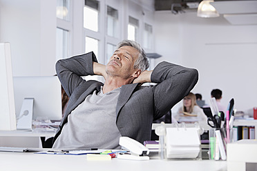 Germany, Bavaria, Munich, Mature man resting, colleagues working in background - RBYF000064