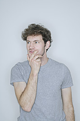 Young man standing with hand on chin against white background - TCF002388