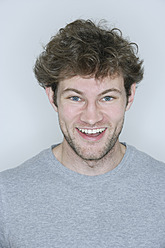 Young man standing against white background, smiling, portrait - TCF002392