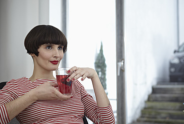 Deutschland, Köln, Junge Frau sitzt mit einem Glas Tee in einer Wohnung - RHYF000052