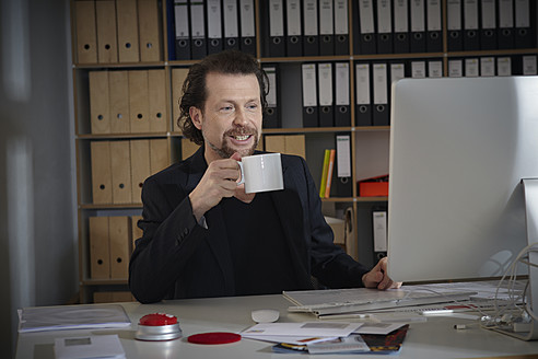 Deutschland, Köln, Älterer Mann mit Kaffeetasse im Büro, lächelnd - RHYF000076