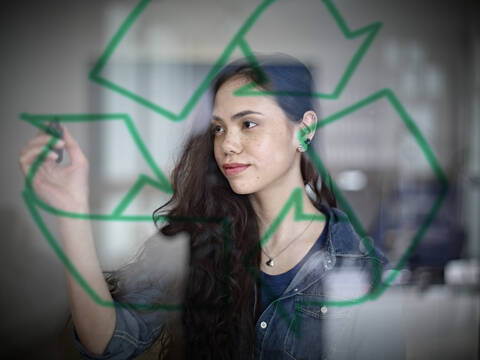 Germany, Cologne, Young woman drawing recycling symbol on glass stock photo