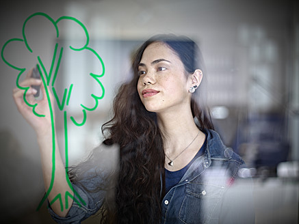 Germany, Cologne, Young woman drawing tree on glass - RHYF000095