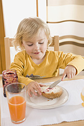 Mädchen bestreicht Brot mit Marmelade, lächelnd - RNF000851