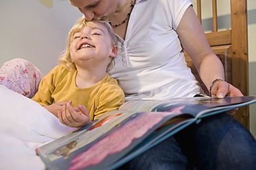 Mutter küsst die Stirn ihrer Tochter und hält ein Buch - RNF000875