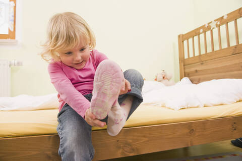 Mädchen sitzt auf dem Bett und stellt Schuhe, lizenzfreies Stockfoto