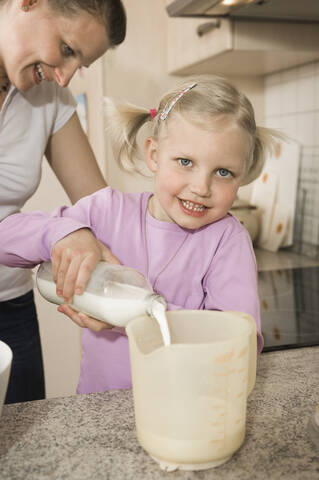 Mutter und Tochter gießen Milch in einen Messbecher, lizenzfreies Stockfoto