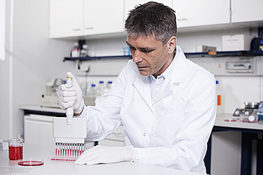 Deutschland, Bayern, München, Wissenschaftlerin gießt rote Flüssigkeit mit Pipette in Testschale für medizinische Forschung im Labor - RBF000818