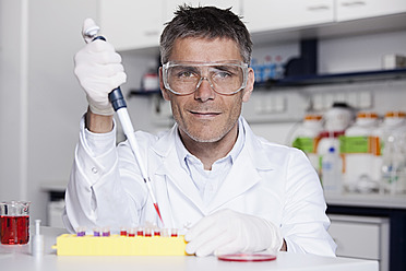 Deutschland, Bayern, München, Wissenschaftlerin gießt rote Flüssigkeit mit Pipette in Reagenzglas für medizinische Forschung im Labor - RBF000831