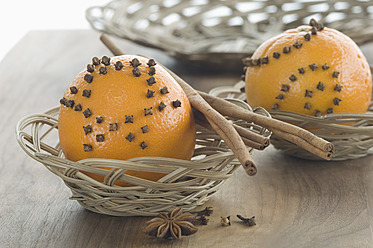 Orange studded with cloves and cinnamon stick in basket besides star anise on table - ASF004546