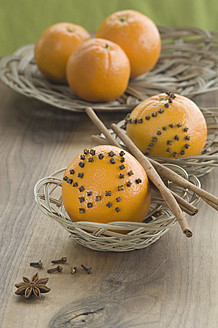 Orange studded with cloves and cinnamon stick in basket besides star anise on table - ASF004547
