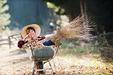 Österreich, Land Salzburg, Junge Frau in Schubkarre mit Herbstlaub, lächelnd - HHF004159