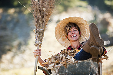 Österreich, Land Salzburg, Junge Frau in Schubkarre mit Herbstlaub, lächelnd - HHF004161