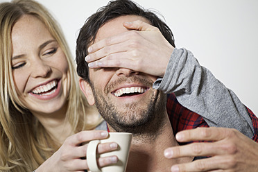 Woman covering eyes of man and holding coffee cup, smiling - FMKF000462