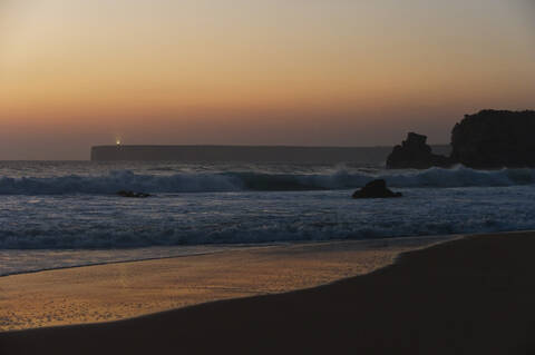 Portugal, Algarve, Sagres, Blick auf Strand mit brechenden Wellen bei Sonnenuntergang, lizenzfreies Stockfoto