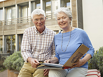 Germany, Cologne, Senior couple with photo album in front of nursing home, portrait - WESTF018657