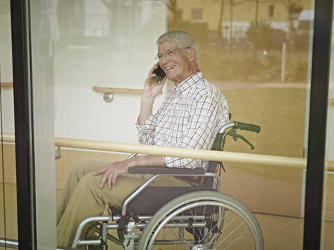 Deutschland, Köln, Älterer Mann am Telefon im Pflegeheim, lächelnd, lizenzfreies Stockfoto