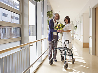 Deutschland, Köln, Ältere Frau und Hausmeisterin mit Blumenstrauß in der Hand und lächelnd an einem Rollator stehend - WESTF018695