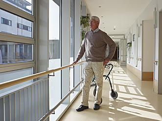 Germany, Cologne, Senior man standing in corridor of nursing home, walking frame in background - WESTF018699