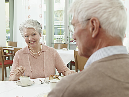 Deutschland, Köln, Älteres Paar sitzt am Tisch, lächelnd - WESTF018710