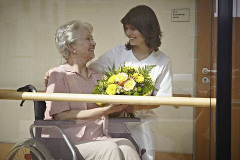 Germany, Cologne, Caretaker giving bouquet to senior women on wheelchair in nursing home stock photo