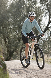 Italy, Trento, Mid adult woman cycling through dirt track - DSF000573