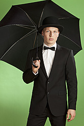 Young man holding umbrella against green background - MAEF004654