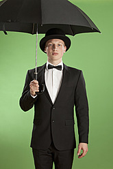 Young man holding umbrella against green background - MAEF004655