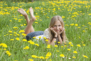 Österreich, Jugendliches Mädchen liegend im Blumenfeld, Porträt - WWF002373