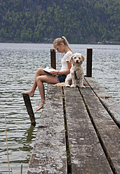 Österreich, Jugendliches Mädchen liest Buch neben Hund auf Steg - WWF002383