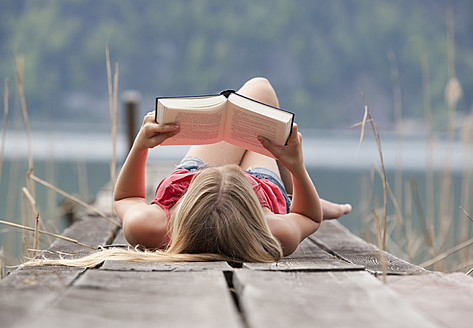 Austria, Teenage girl lying and reading book on jetty - WWF002386