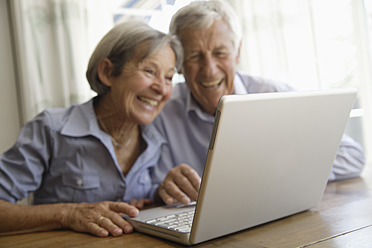 Germany, Bavaria, Senior couple using laptop at home, smiling - TCF002592