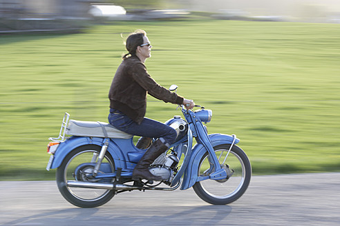 Germany, Bavaria, Mature woman riding old moped of 1960s - TCF002604